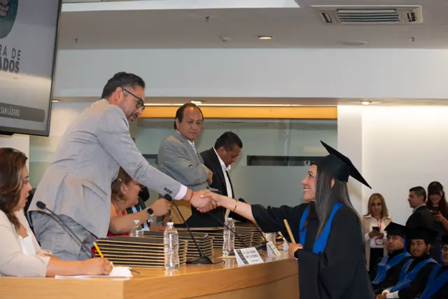 Graduada sonriente estrecha la mano de un presentador al recibir su título.