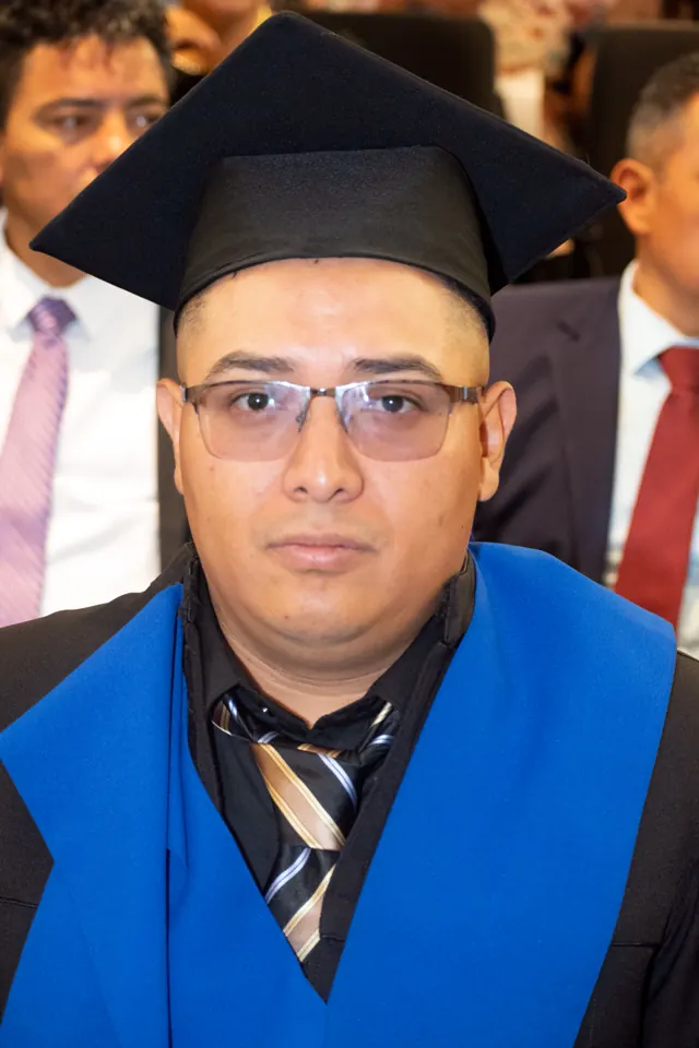 Retrato de un graduado con lentes, birrete negro, estola azul y corbata a rayas.