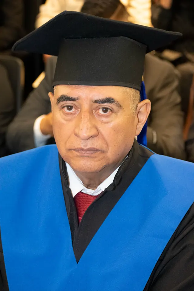 Graduado con birrete negro y estola azul sentado entre los asistentes a la ceremonia.