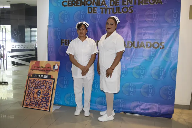 Dos integrantes de la comunidad frente al fondo de graduación. Graduación del 7 de julio de 2025.