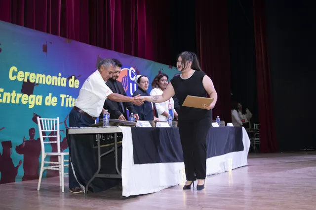 Graduada con vestido negro recibe su documento en el escenario. Graduación del 7 de julio de 2025.