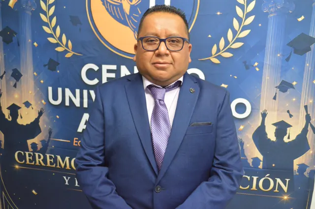 Participante con lentes, traje azul y corbata lila posa frente al fondo de la graduación.