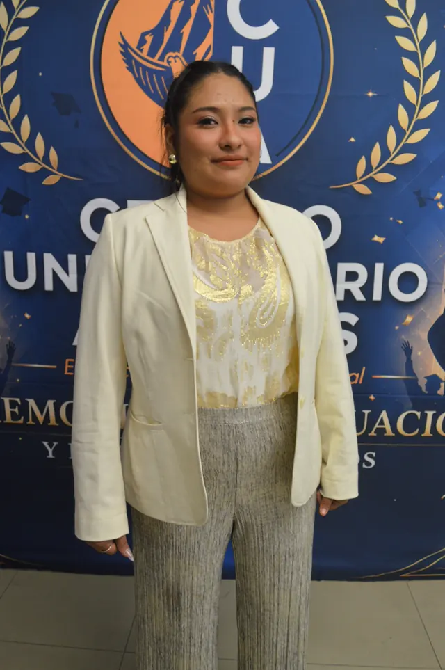 Participante sonriente con saco claro posa frente al fondo de graduación de Acacias.