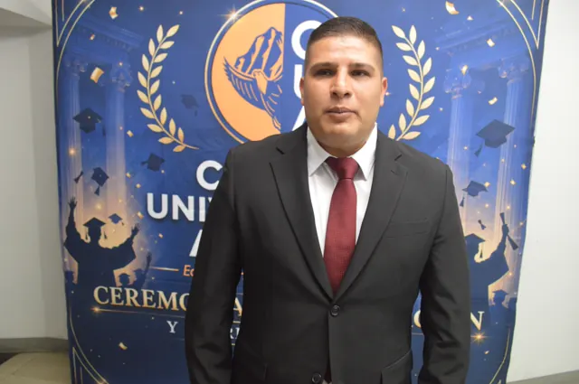 Participante con traje negro y corbata roja posa ante el fondo de graduación de Acacias.