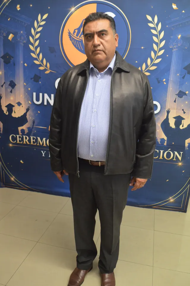 Participante con chaqueta negra y camisa a rayas posa ante el fondo de graduación.