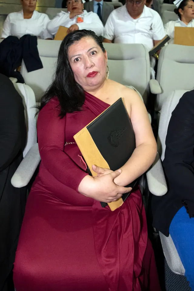 Asistente con vestido color vino sostiene su carpeta durante la ceremonia. Graduación del 14 de junio de 2025.