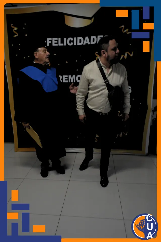 Graduado comparte un momento con un acompañante frente al fondo de la ceremonia. Graduación del 14 de junio de 2025.